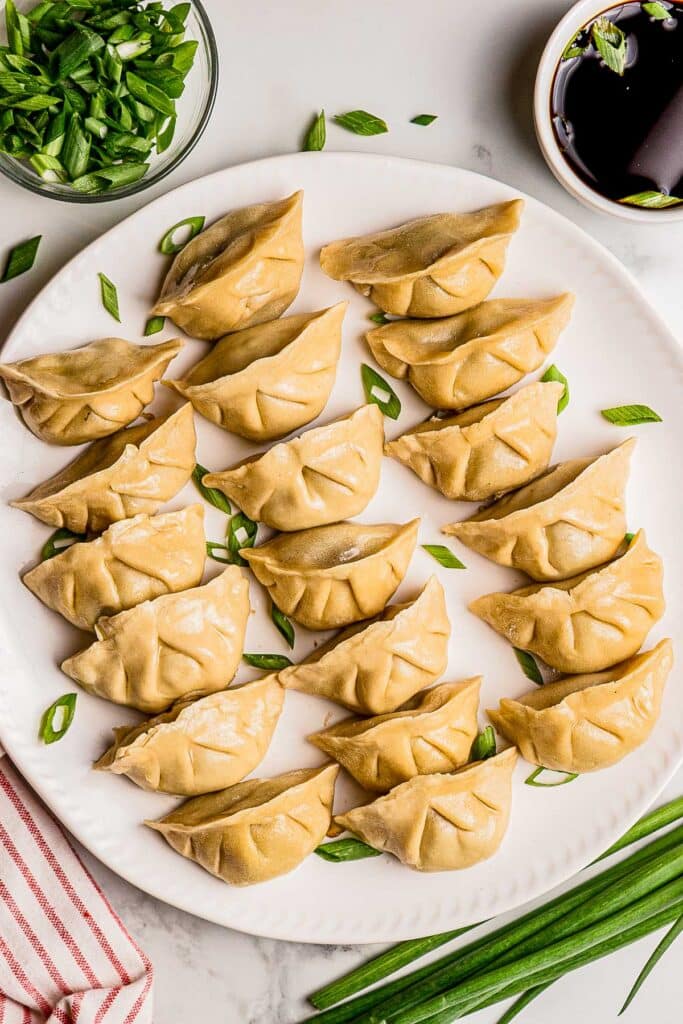 overhead view of white platter filled with ginger beef dumplings with small bowls of green onions and chopped green onions on the side
