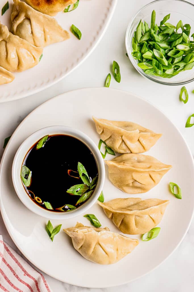 overhead view of four beef Asian dumplings on white plate with bowl of soy sauce and sliced green onions
