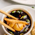 chopsticks holding ground beef dumpling over bowl of soy sauce