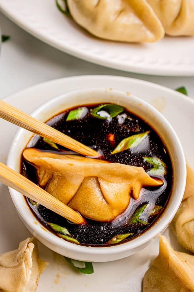 chopsticks holding ground beef dumpling over bowl of soy sauce