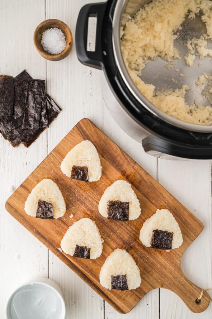 formed onigiri with nori sheets placed on bottom next to instant pot