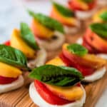 closeup view of wooden cutting board with stacks of mozzarella, tomatoes, peaches, and basil drizzled with balsamic vinegar