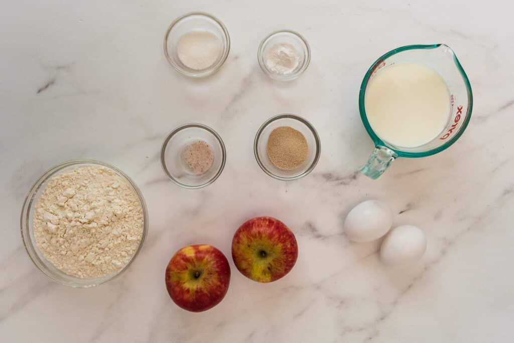 ingredients for apple pancakes in glass bowls on marble counter