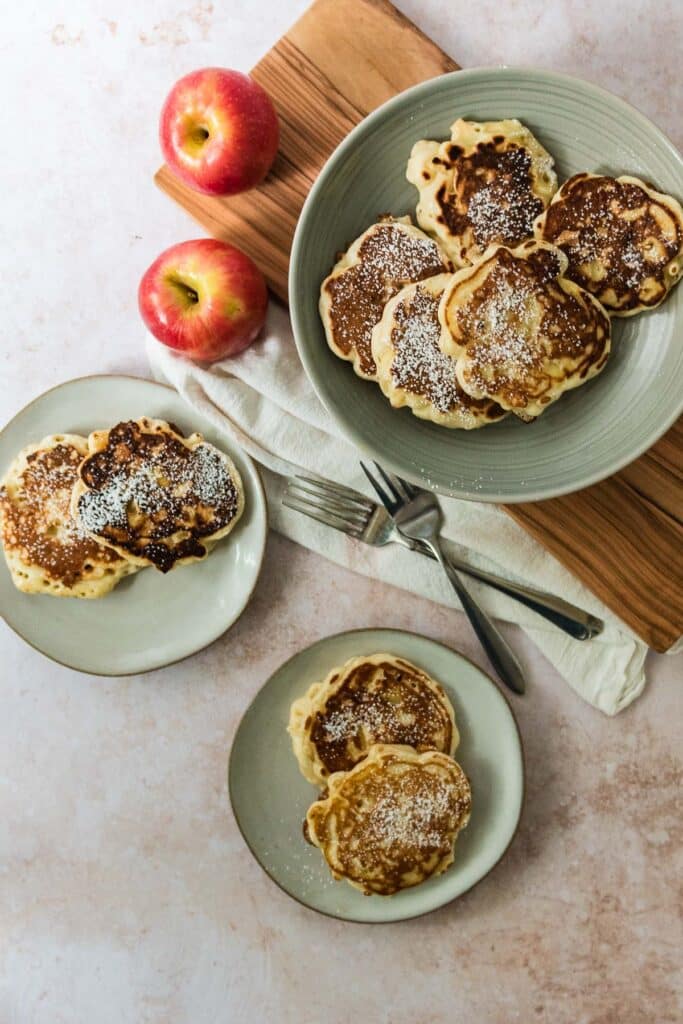 overhead image of two grey plates with apple pancakes next to platter with more pancakes and apples