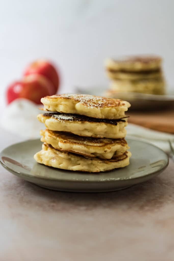 stack of four polish apple pancakes on grey plate with second plate with stack and two apples in background